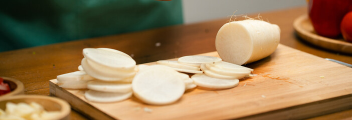 Hands slicing Radish on a wooden board in the kitchen, preparing to cook.