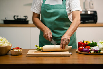 Hands slicing Radish on a wooden board in the kitchen, preparing to cook.