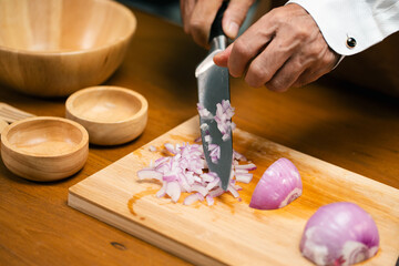 Close up of hands slicing onion on cutting board in kitchen.