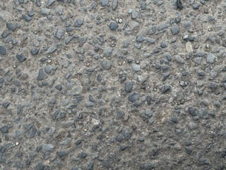 Close-up of rough asphalt pavement with visible stones and gravel, forming a textured background.