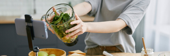 Person preparing a healthy smoothie in a blender while filming a vlog in the kitchen