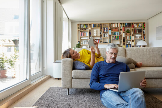 Couple relaxing with digital devices in a bright living room - Powered by Adobe