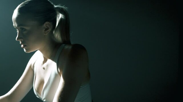 Kopbieta trenujaca na rowerze stacjonarnym w zaciemnionej salki w oswietleniem filmowym 