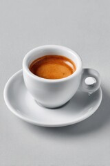 Fototapeta premium A single espresso shot in a small, white cup and saucer, set against a light grey background; the crema is visible