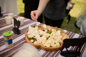 People take cheese cut into cubes from a wooden plate on a tablecloth with an ornament