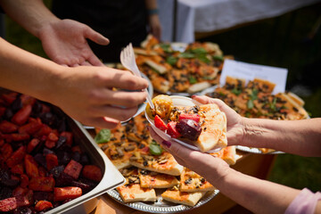 Hands of people taking food from a plastic plate during a banquet