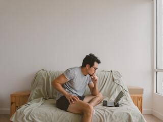 Asian man sitting on bed stretching lower back in pain in white shirt and clean background