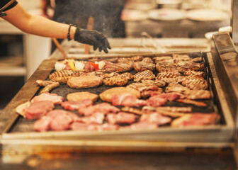 Assorted meats grilling on a large flat-top grill during busy restaurant service. Gloved hand...