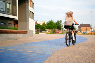 girl riding bicycle in urban neighborhood, wearing backpack and school uniform, pedaling along blue...