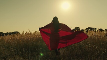 happy girl play superheroes they run across green field in red cloak, cloak flutters in wind. children's games and dreams. Slow motion. teenager dreams of becoming superhero. young girls in red cloak.