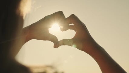 A girl shows her heart with her hands at sunset, a tourist trip, a romantic health vacation, dreaming to love life, an active lifestyle, a dream of a happy relationship with a loved one.