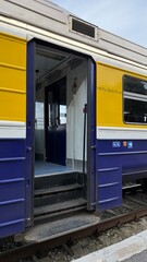 Open train door of a yellow, blue passenger carriage at Daugavpils railway station, Latvia, on July 6, 2025. The entrance shows a step into the interior of a DR1A-series diesel train used on regional 