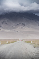 Landscape of mountain peaks and ridges with rocks and snow, in the Tien Shan mountain system in Pamir, cloudy weather and the asphalt road of the Pamir Highway going into the distance