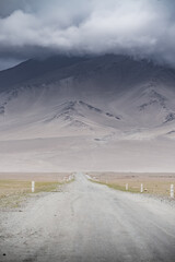 Landscape of mountain peaks and ridges with rocks and snow, in the Tien Shan mountain system in Pamir, cloudy weather and the asphalt road of the Pamir Highway going into the distance
