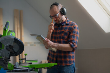 A white male carpenter, aged 35-40, wearing safety glasses, measuring his next cut on a miter saw...