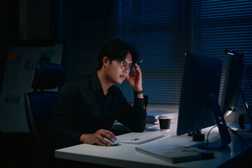 Focused businessman working late at night, staring at computer monitor in a dark office
