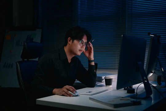 Focused businessman working late at night, staring at computer monitor in a dark office
