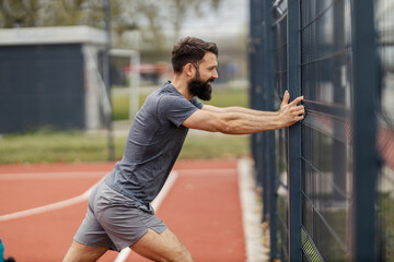 Side view of sportsman doing strength exercises against the fence.