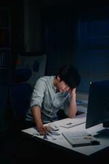 Fototapeta premium Man working late at night in a dim office, showing signs of stress and fatigue at his desk