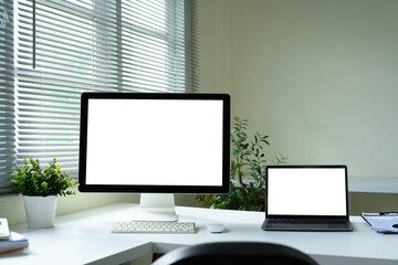 Modern home office with desktop monitor and laptop, both displaying blank white screens