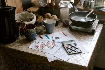 Kitchen table holding overdue bills marked pass due, calculator, eyeglasses, mugs, bread and frying...