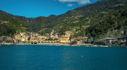Monterosso al Mare, Cinque Terre, colorful buildings, fortress towers nestled between terraced cliffs above Ligurian Sea.