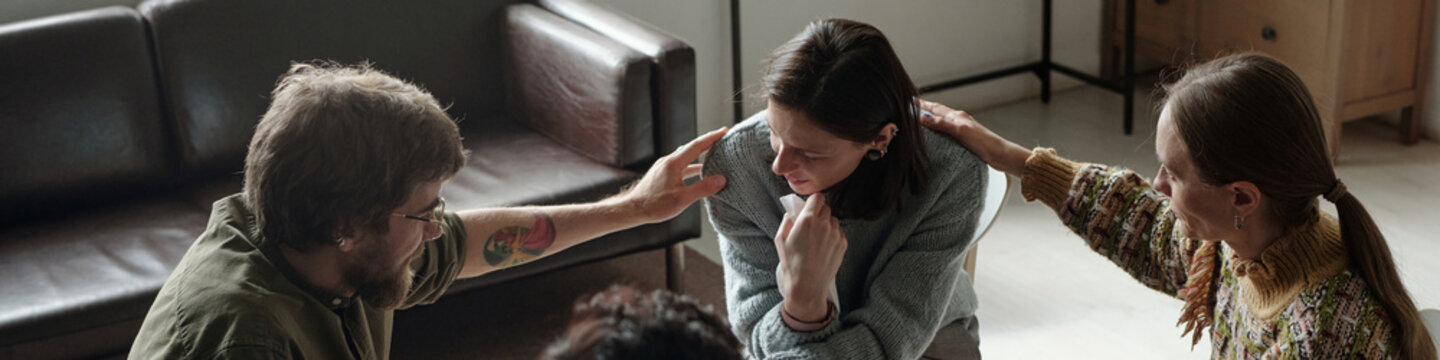 Woman sitting in therapy session receiving comfort from man and woman, group supporting each other indoors