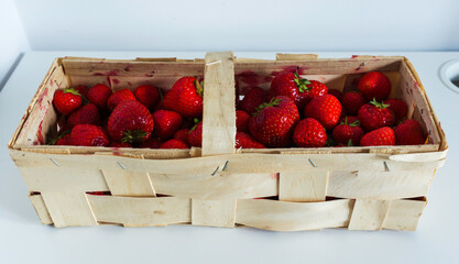 Juicy ripe strawberries in a rustic wooden basket on a white table. Healthy summer fruit, freshly...