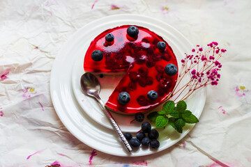 Delicious red jelly cake with raspberries and blueberries served on a white plate with a spoon,...