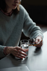 Woman sitting at table holding eyeglasses in one hand glass of water in other hand during therapy session focusing on mental health support