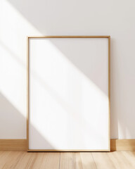 Blank poster mockup in wooden frame on white wall above a desk. Minimalist Scandinavian interior, natural light and soft shadows, clean layout.