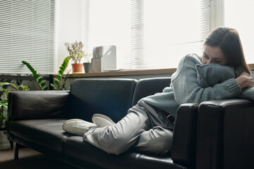 Woman lying on sofa hugging pillow, appearing contemplative during therapy session in modern...