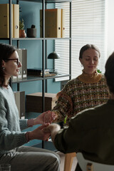 Woman sitting in therapy session holding hands with woman and man participating in group support...