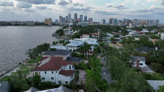 Establishing drone flight over bayshore of Tampa City with luxury houses between rivers. Skyline of downtown with skyscrapers in background. Flyover shot. Florida, United States.