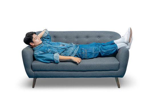 A young man daydreams while lying on a sofa, looking up with a thoughtful and relaxed expression.
