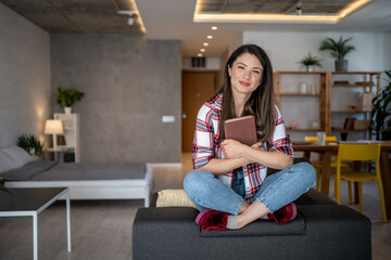 Young woman relaxing on sofa holding a book in modern apartment