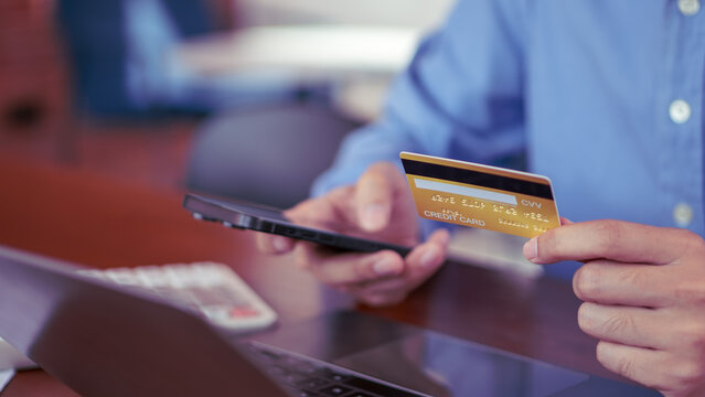 Man holding a gold credit card and smartphone while shopping online, showcasing secure mobile payment, digital transactions, and modern finance in an office environment.