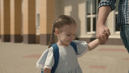 Dad leads the child by hand to school, close-up, a little schoolgirl with backpack, a happy family,...