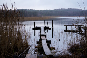 Spooky small wooden pier leading into grey lake on an rainy overcast day with forest in the background