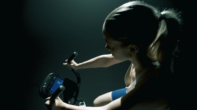 Widok z g&oacute;wy na kobiete trenujaca na rowerze stacjonarnym na zaciemnionej siłowni w swietle filmowym 