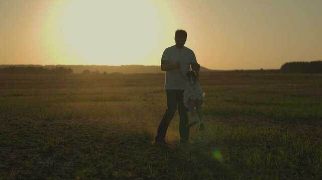 dad is circling little daughter at sunset, silhouette of father and child against sky, happy family, childhood dream, to love and play with kid, girl with parent is playing cheerfully, trip to nature.