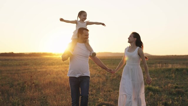 happy family, mother, father and little child, kid sits on shoulders dad, childhood dream of flying, parents with their daughter run at sunset, adult man and woman laugh playing with baby in sunlight. - Powered by Adobe