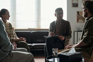 Man conducting therapy session with two adults and one woman sitting in circle discussing mental...