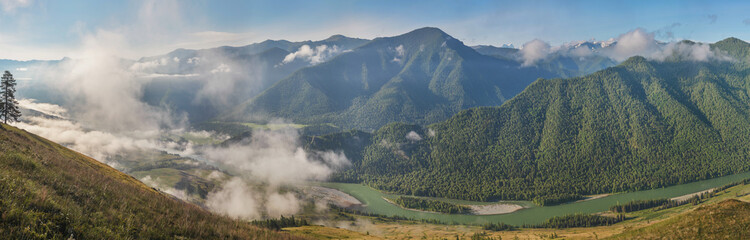 Mountain valley with river in the morning light, mist and green of forests and meadows, panoramic...