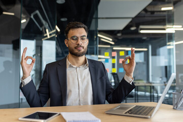 A businessman meditates in an office, showing relaxation and mindfulness for stress relief and...
