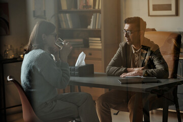 Woman sitting across from man wearing glasses, engaging in therapy session, man listening...