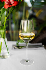 Elegant glass of white wine on a restaurant table with red flowers in the background, evoking a refined and romantic dining ambiance
