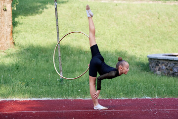 Gymnast performs graceful split standing with a hoop surrounded by lush greenery, showcasing...