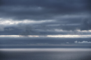 Moody cloudy sky over a dark ocean horizon with a band of light