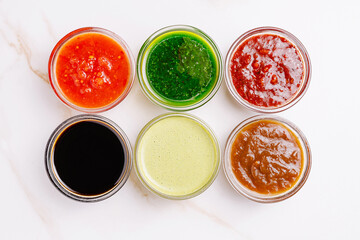Colorful assortment of sauces in glass jars on white background